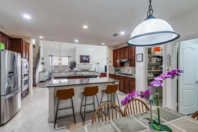 a kitchen with stainless steel appliances kitchen island granite countertop a dining table chairs refrigerator and cabinets