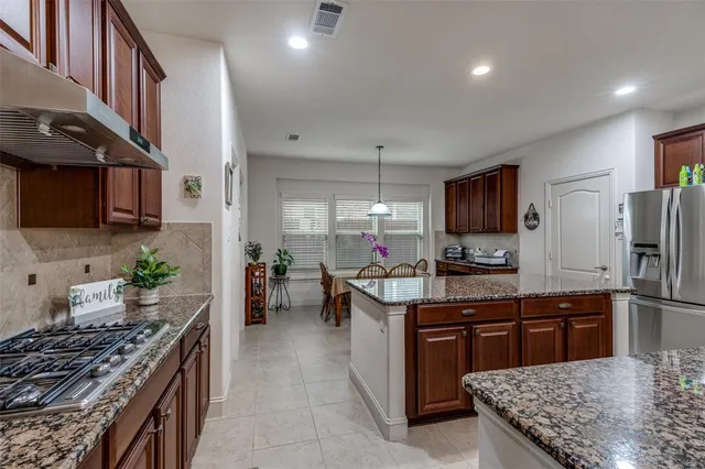 a kitchen with stainless steel appliances granite countertop a stove top oven a sink dishwasher a dining table and chairs with wooden floor