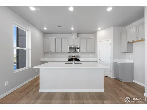 a living room with stainless steel appliances granite countertop a sink a microwave a refrigerator and white cabinets with wooden floor