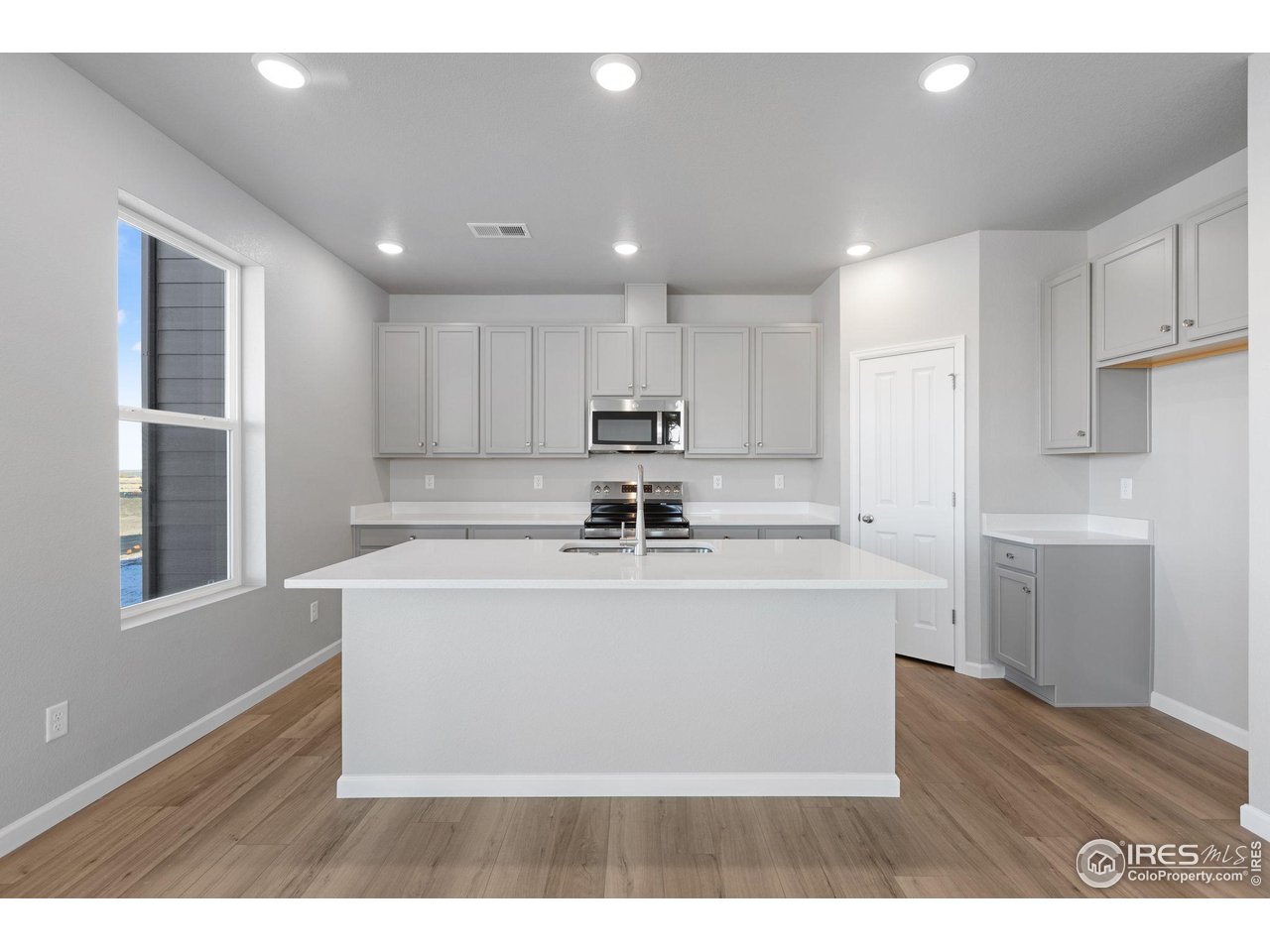 6765 Utica Court Firestone, CO 80504 - Photo 6 of 23 a living room with stainless steel appliances granite countertop a sink a microwave a refrigerator and white cabinets with wooden floor