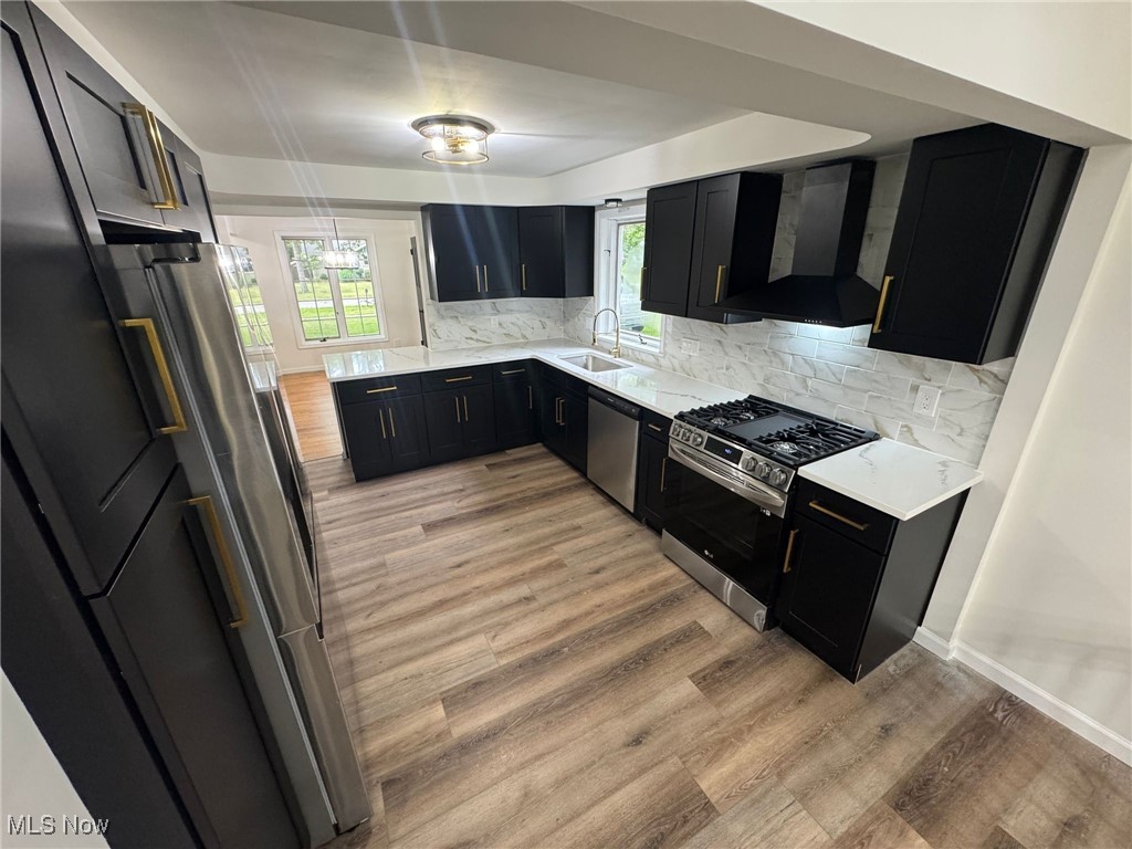 4018 Root Road North Olmsted, OH 44070 - Photo 6 of 23 Kitchen featuring appliances with stainless steel finishes, wall chimney exhaust hood, dark cabinets, light wood-style floors, and plenty of natural light
