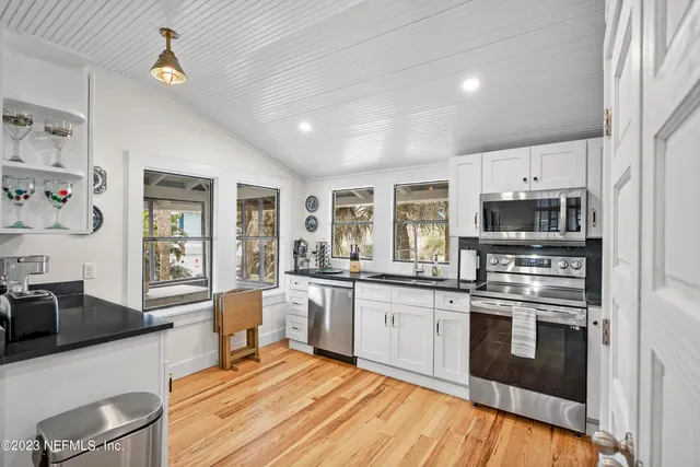 a large kitchen with stainless steel appliances granite countertop a stove top oven a sink dishwasher a dining table and chairs with wooden floor