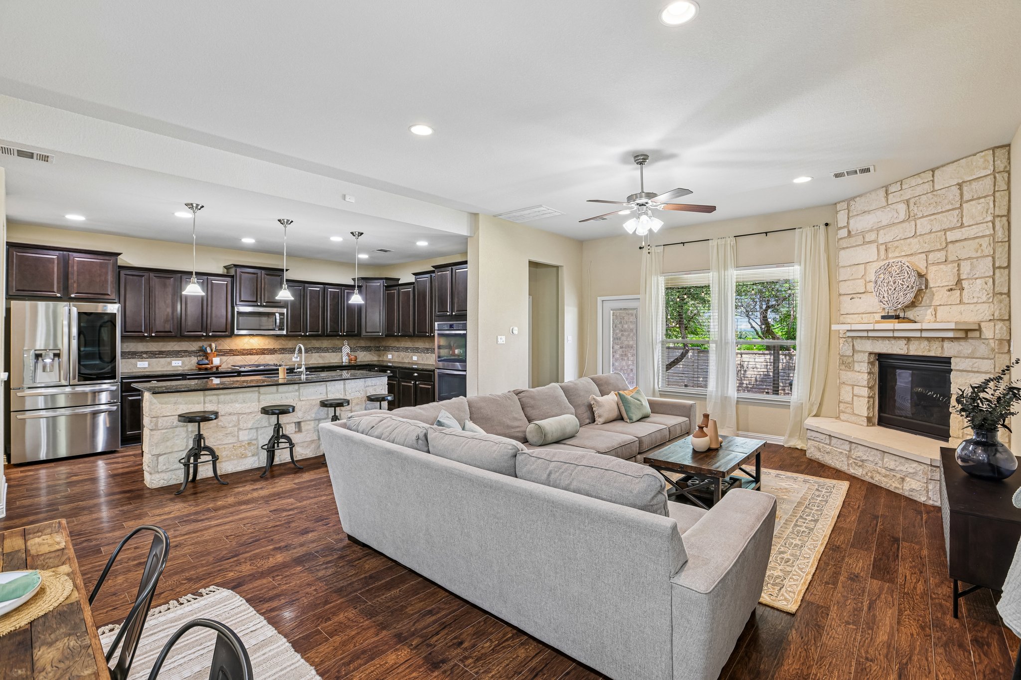 1924 Granite Springs Road Leander, TX 78641 - Photo 6 of 36 An inviting open-concept layout unites the kitchen and living area, highlighted by a stone fireplace and rich hardwood flooring.