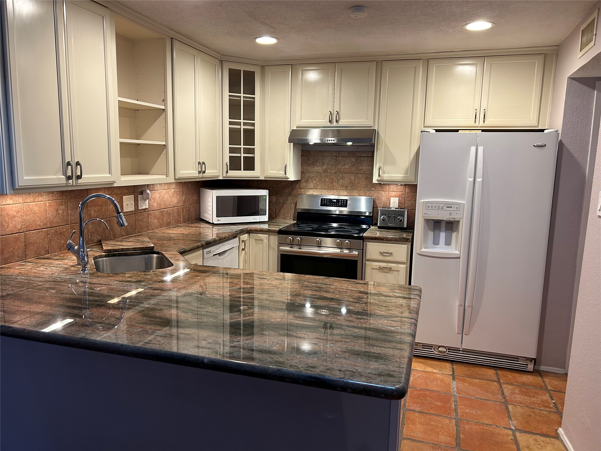 13034 Leader Street, Unit 965 Houston, TX 77072 - Photo 10 of 32 This kitchen includes a large refrigerator, a corner sink, countertop microwave and an electric stove, with warm-toned tiles adding a cozy touch.