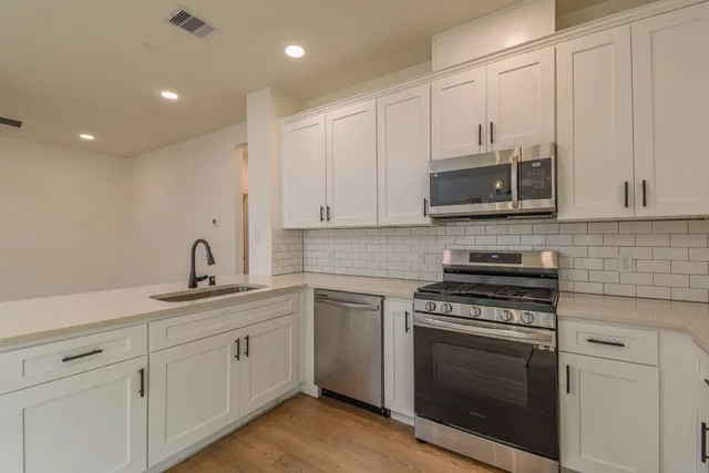 a kitchen with cabinets stainless steel appliances a sink and wooden floor