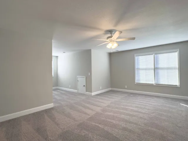 an empty room with chandelier fan and windows