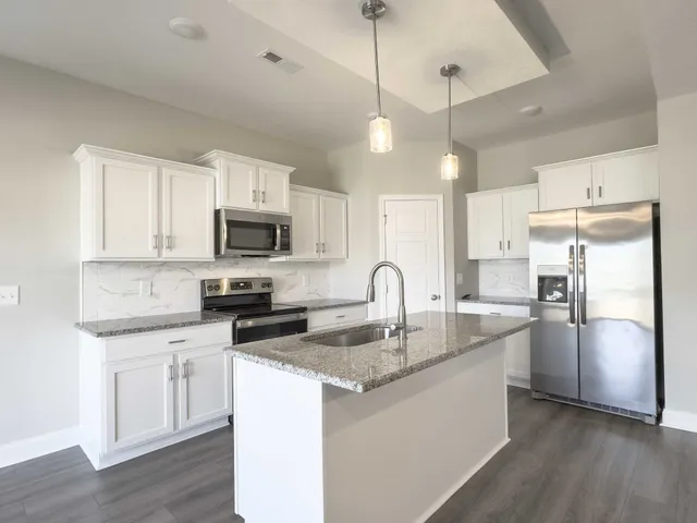 a kitchen with stainless steel appliances granite countertop a refrigerator a sink dishwasher a stove and white countertops with wooden floor