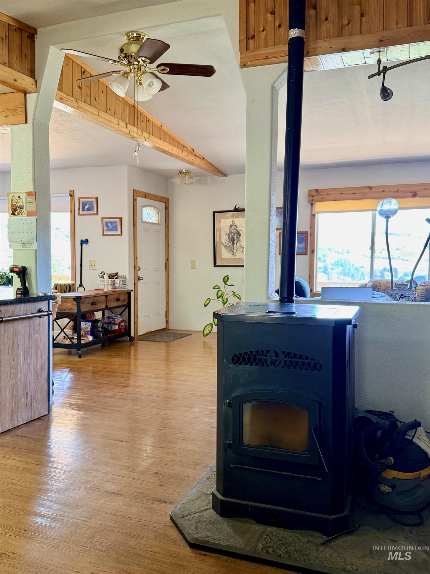 35322 River Road Lenore, ID 83541 - Photo 7 of 42 Freestanding wood-burning stove with a stone hearth, set within a living area featuring wood-finish flooring, exposed wood beams, and a ceiling fan