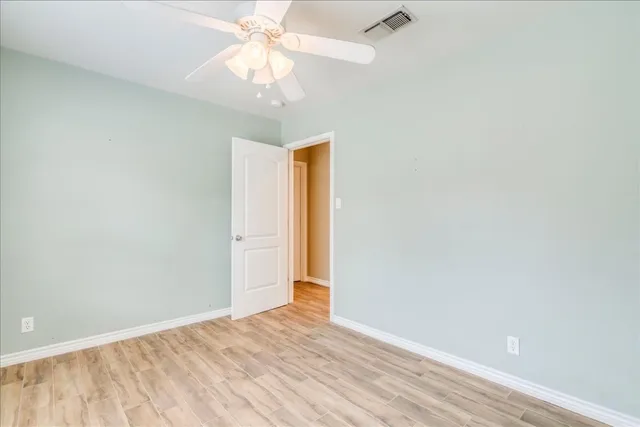 an empty room with a chandelier fan and wooden floor
