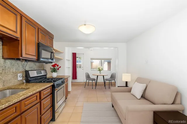 a living room with stainless steel appliances furniture a rug and a kitchen view
