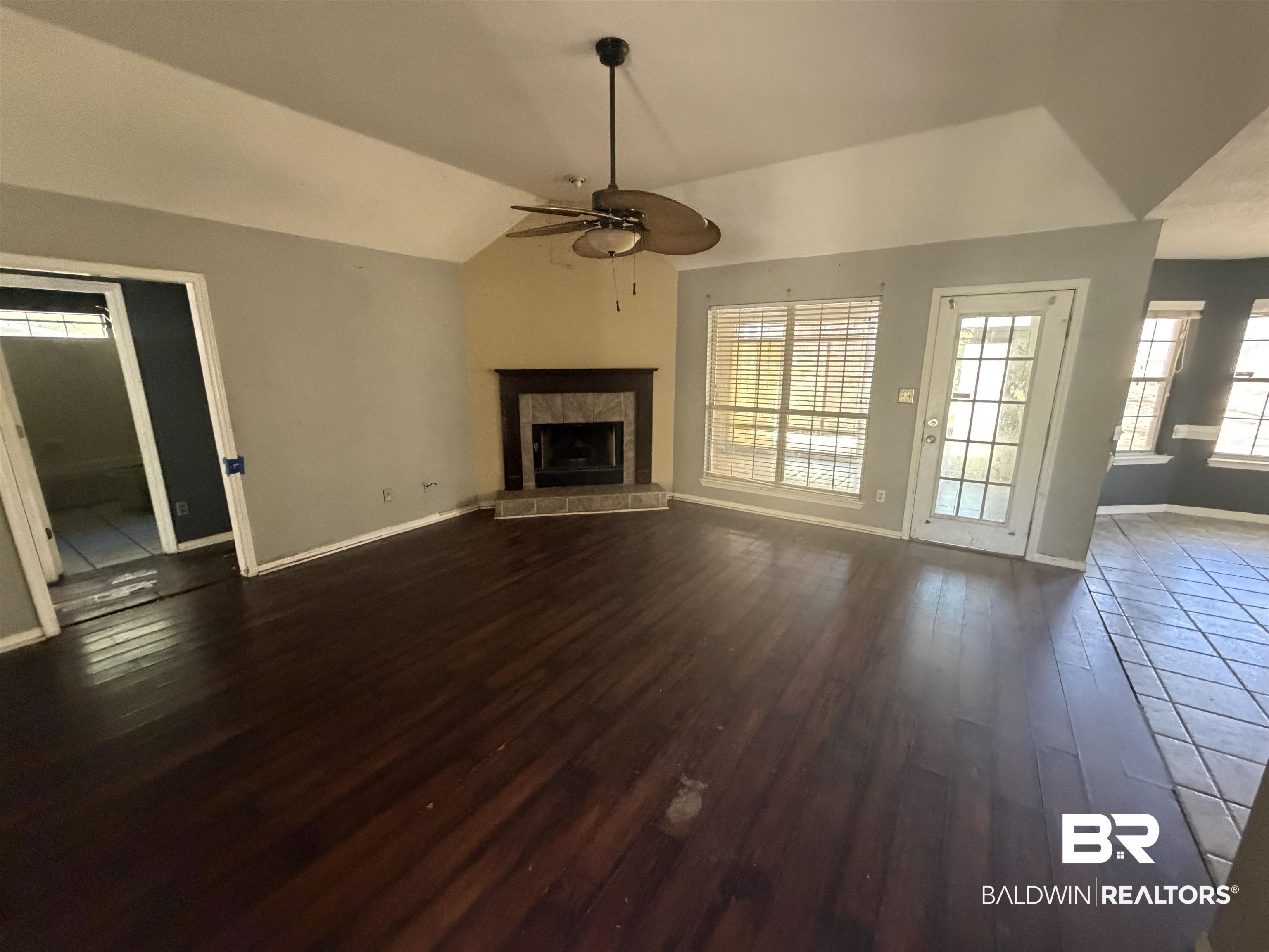 7067 Pinehill Road Daphne, AL 36526 - Photo 10 of 18 Unfurnished living room with dark wood-style floors, vaulted ceiling, a tiled fireplace, and ceiling fan
