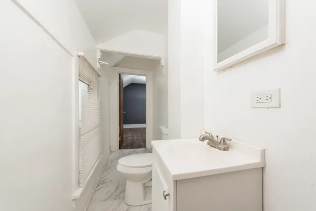 an empty room with wooden floor and way to kitchen