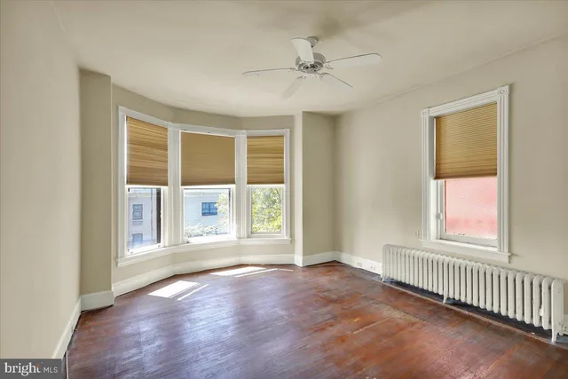 an empty room with wooden floor fan and windows