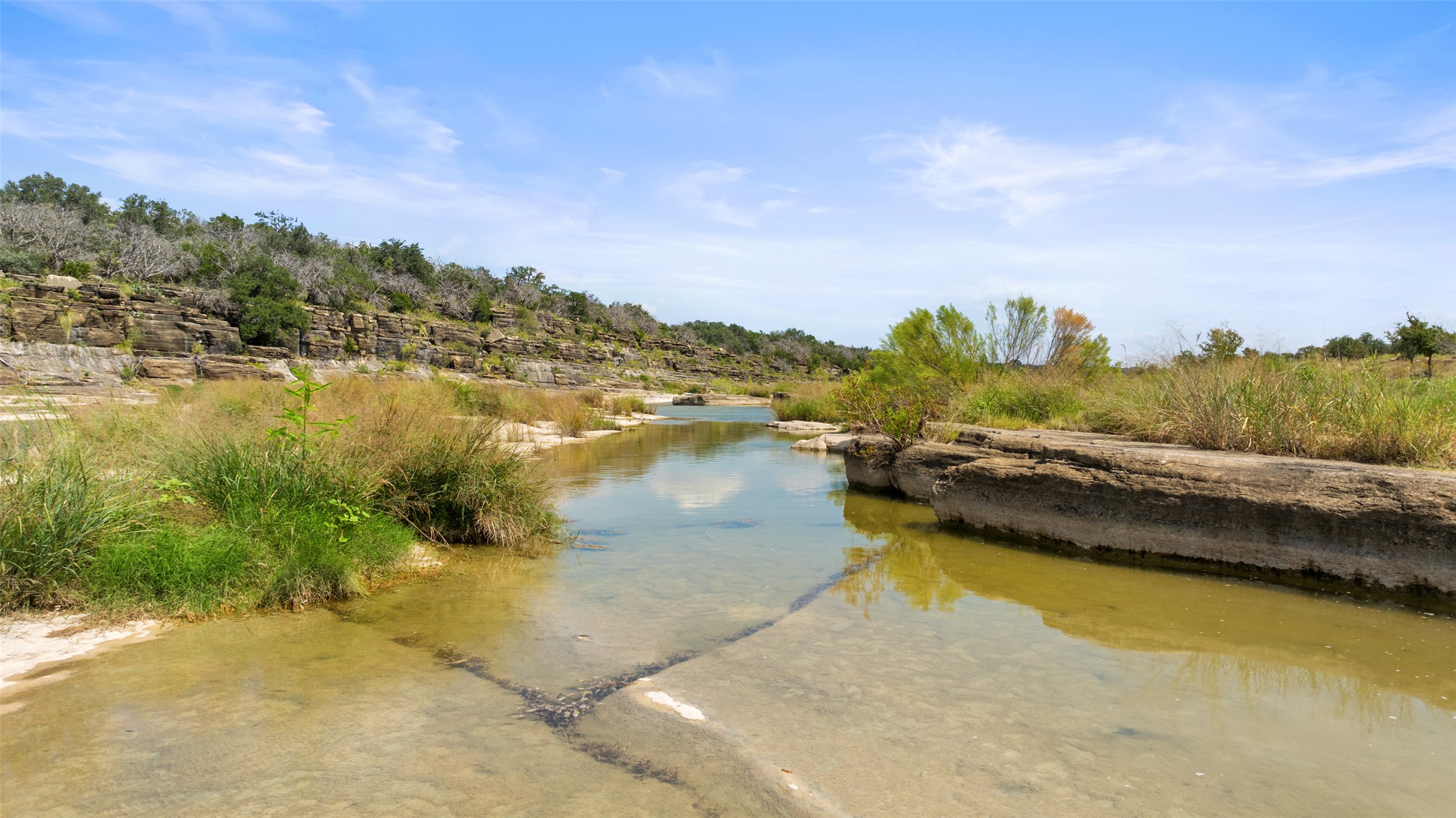 960 Gibson Road Johnson City, TX 78636 - Photo 8 of 19 A tranquil stream meanders through a rugged landscape, framed by natural rock formations and lush greenery.
