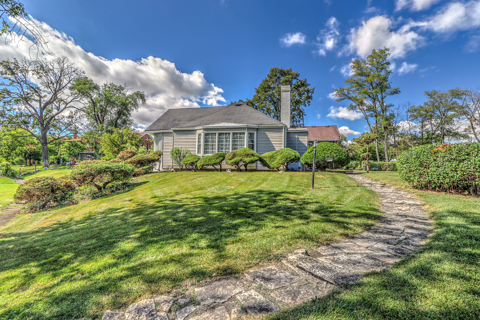 a view of house in front of a big yard with large trees