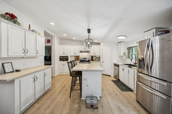 a kitchen with stainless steel appliances kitchen island granite countertop a refrigerator a sink dishwasher a stove and white cabinets with wooden floor
