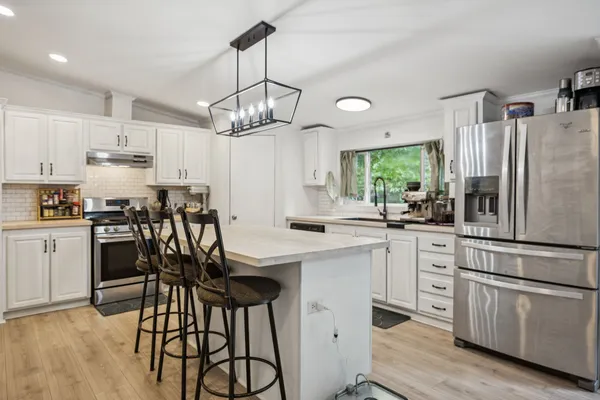 a kitchen with stainless steel appliances a dining table chairs refrigerator and cabinets