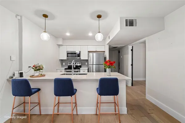 a kitchen with stainless steel appliances kitchen island granite countertop a dining table chairs and a refrigerator