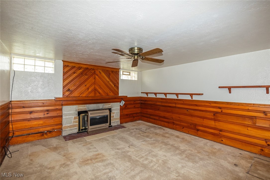 7494 Brecksville Road Independence, OH 44131 - Photo 14 of 20 Unfurnished living room featuring a stone fireplace, a textured ceiling, a textured wall, carpet, and a ceiling fan