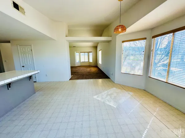 a view of an empty room with a window and kitchen view