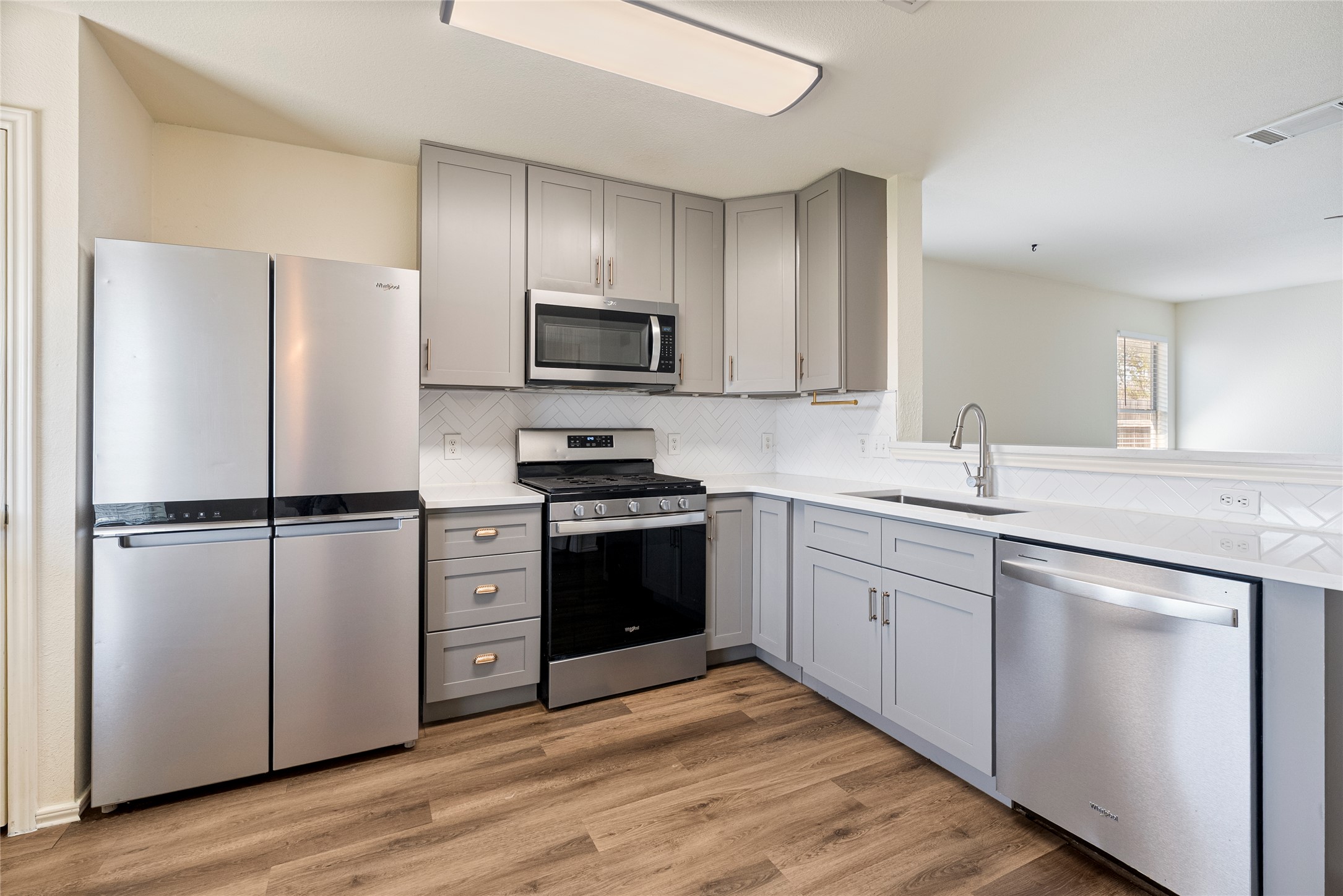 348 Atlantis Kyle, TX 78640 - Photo 11 of 17 Kitchen featuring gray cabinetry, stainless steel appliances, light wood-type flooring, decorative backsplash, and a peninsula