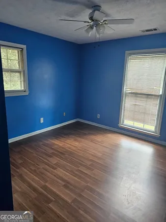 an empty room with wooden floor fan and windows