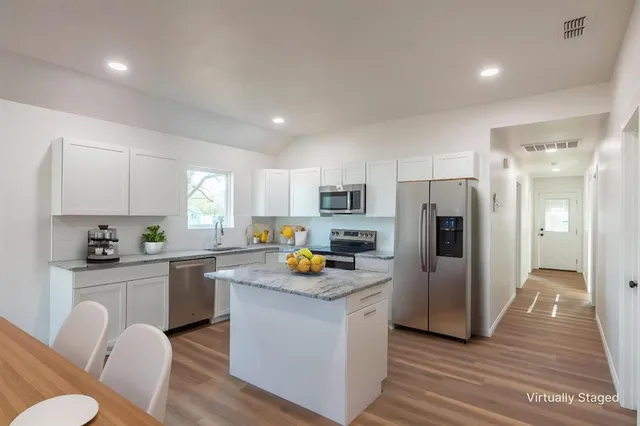 a kitchen with stainless steel appliances a refrigerator a stove a sink dishwasher and white cabinets with wooden floor