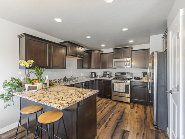12214 Sunpark Lane Draper, UT 84020 - Photo 7 of 24 Kitchen featuring dark wood finish cabinetry, stainless steel appliances, light stone counters, a peninsula, and recessed lighting