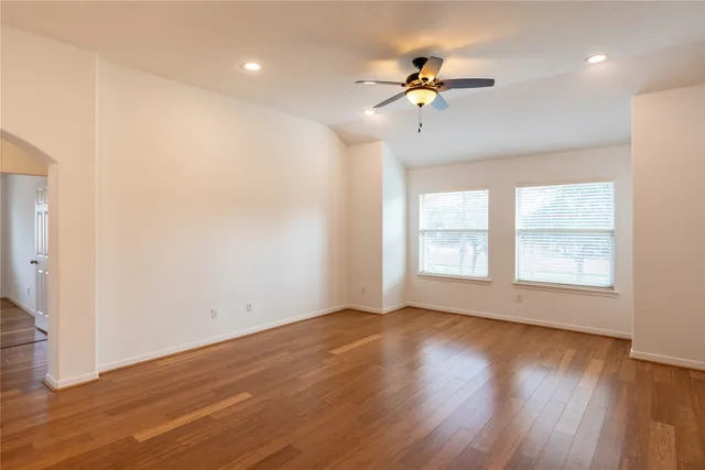 an empty room with wooden floor ceiling fan and windows