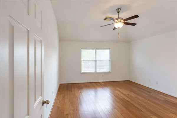 an empty room with wooden floor fan and windows