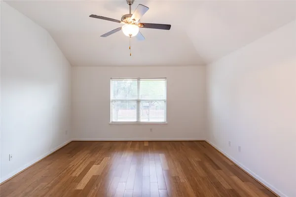 an empty room with wooden floor ceiling fan and windows