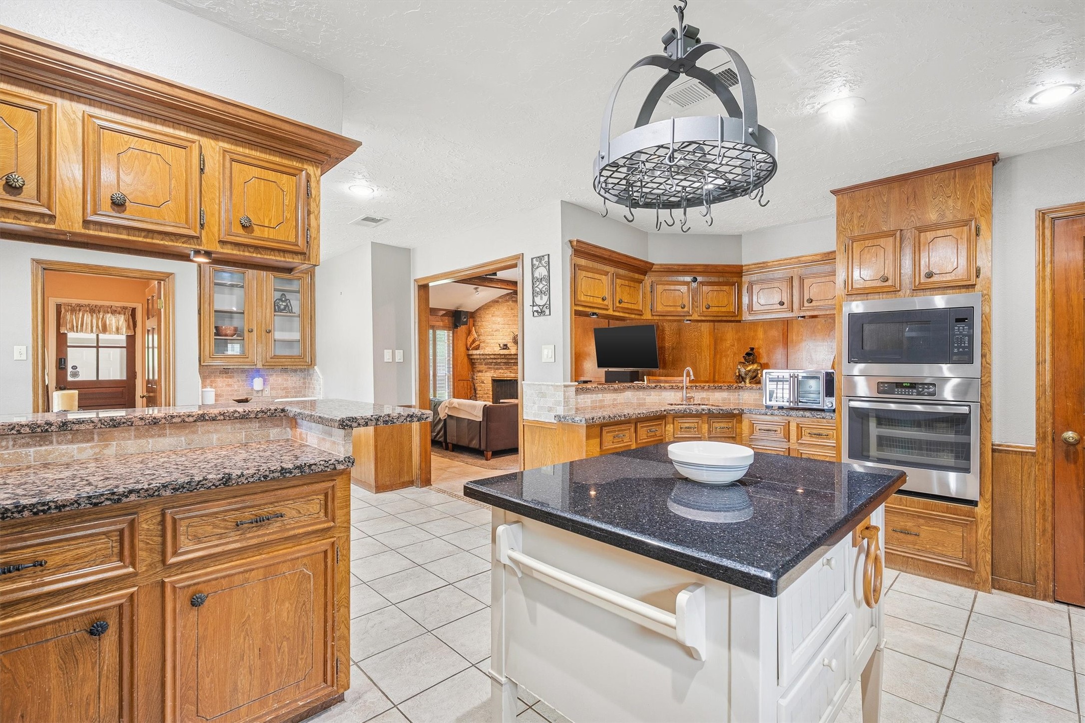 826 North Rivershire Drive Conroe, TX 77304 - Photo 16 of 46 The stainless built-in single oven and microwave, pot rack chandelier, and granite island tell you this kitchen means business. And that sightline into the living room with the fireplace beyond? That is open concept done right.