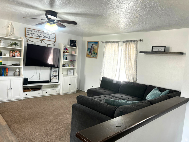 570 250 East Parowan, UT 84761 - Photo 2 of 27 Living area featuring neutral wall tones, textured ceiling, a ceiling fan with integrated lighting, and a large window with curtain rods