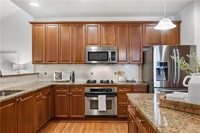 a kitchen with stainless steel appliances granite countertop a stove a sink dishwasher and a refrigerator with wooden cabinets