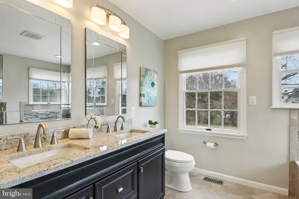 a bathroom with a granite countertop toilet a sink a mirror a and a window