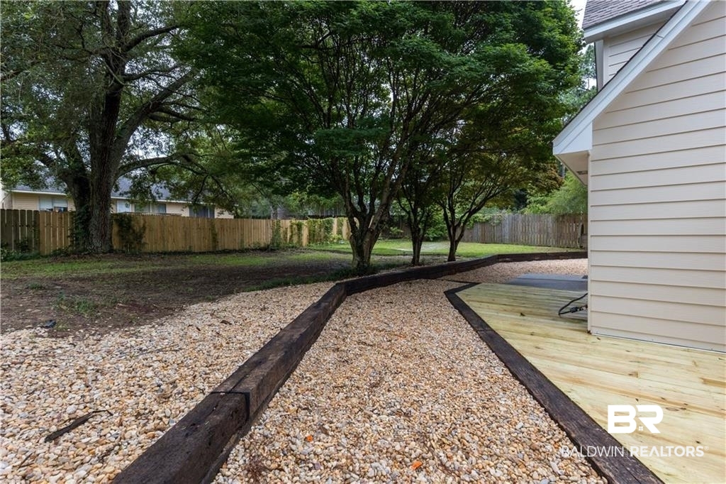 101 Lawson Road Daphne, AL 36526 - Photo 19 of 20 Rear yard featuring a newly installed wood deck, gravel pathway, mature trees, and a privacy fence