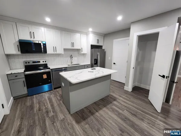 a kitchen with stainless steel appliances a sink dishwasher a refrigerator a stove top oven a wooden floor and cabinets