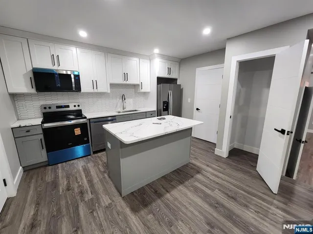 a kitchen with stainless steel appliances a sink dishwasher a refrigerator a stove top oven a wooden floor and cabinets