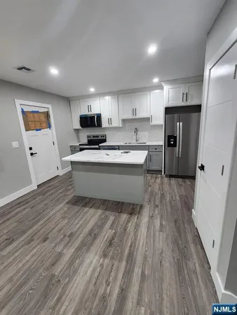 a kitchen with stainless steel appliances granite countertop a refrigerator a sink dishwasher a stove and white countertops with wooden floor