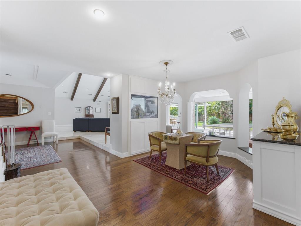 6160 Spring Valley Road Dallas, TX 75240 - Photo 14 of 40 Expansive interior featuring wood-finish flooring, a tiered living space, arched architectural details, a built-in display cabinet, and a crystal chandelier