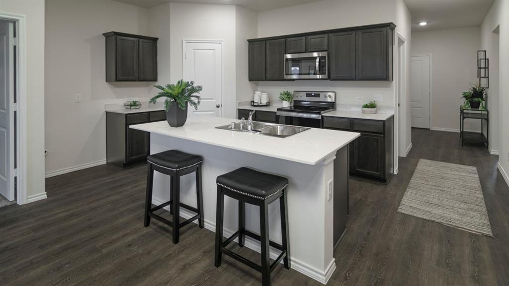 3100 Charleston Drive Ennis, TX 75119 - Photo 9 of 23 Open-concept kitchen featuring dark wood cabinetry, stainless steel appliances, a center island with sink, white countertops, and wood-finish flooring