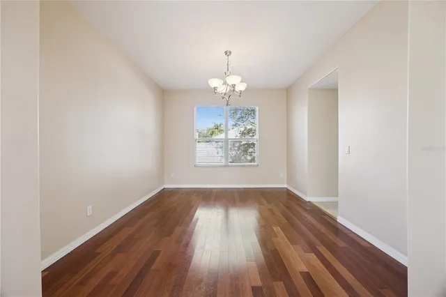 an empty room with wooden floor chandelier and windows