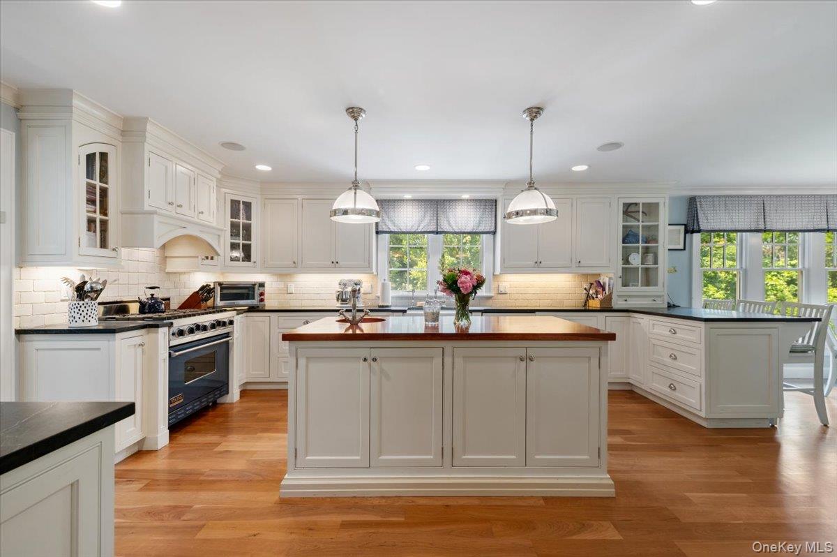 5 Fox Hunt Court Cold Spring Harbor, NY 11724 - Photo 11 of 42 Kitchen featuring white cabinetry, wood-finish flooring, a central island with a wood countertop, black countertops, and a stainless steel range with a visible oven