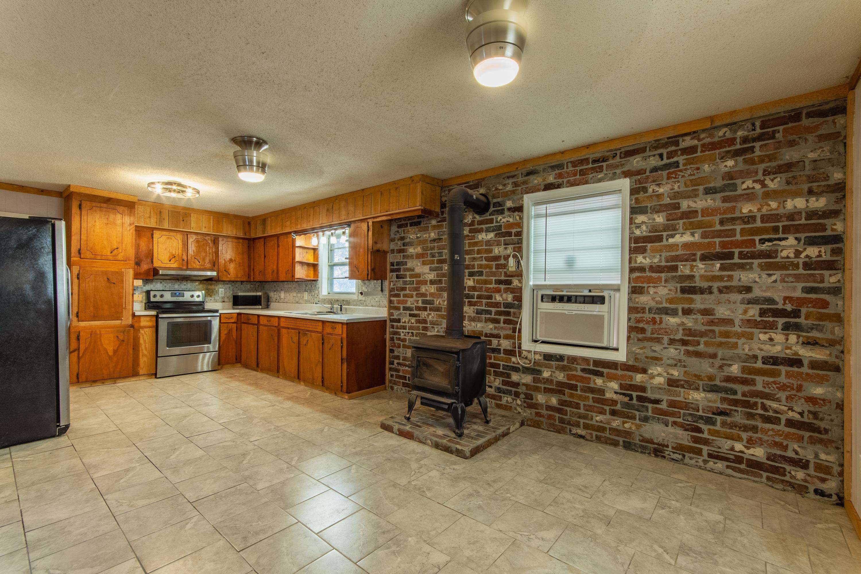 3001 Hamilton Road Ashland, MS 38603 - Photo 23 of 39 Kitchen featuring appliances with stainless steel finishes, tasteful backsplash, brick wall, cooling unit, and a wood stove