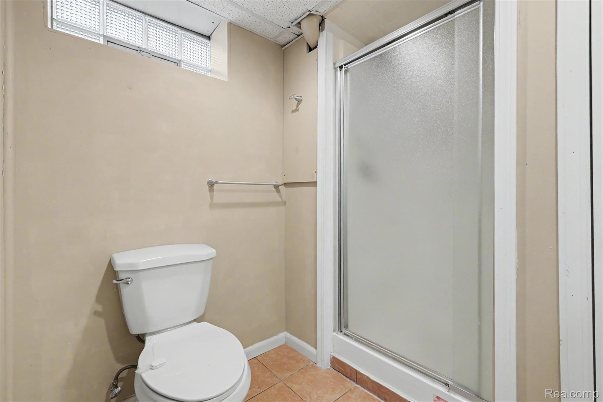 7136 Rosedale Boulevard Allen Park, MI 48101 - Photo 45 of 51 Built-in shower enclosure with frosted glass door, white toilet, and glass block window