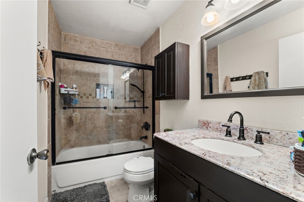7221 Ramona Avenue Rancho Cucamonga, CA 91701 - Photo 18 of 30 a bathroom with a granite countertop sink a toilet a mirror and shower