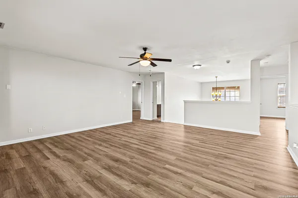 a view of an empty room with wooden floor and a ceiling fan