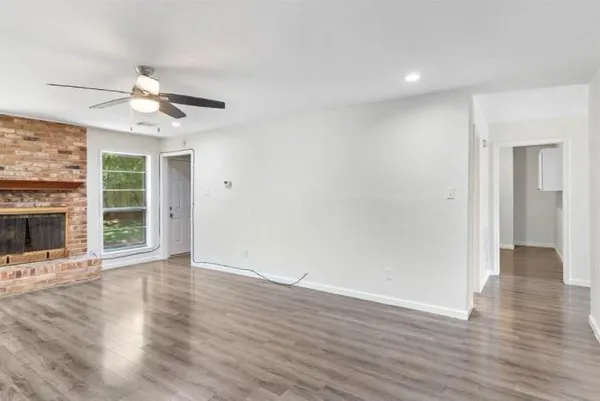 a view of an empty room with wooden floor fireplace and a window