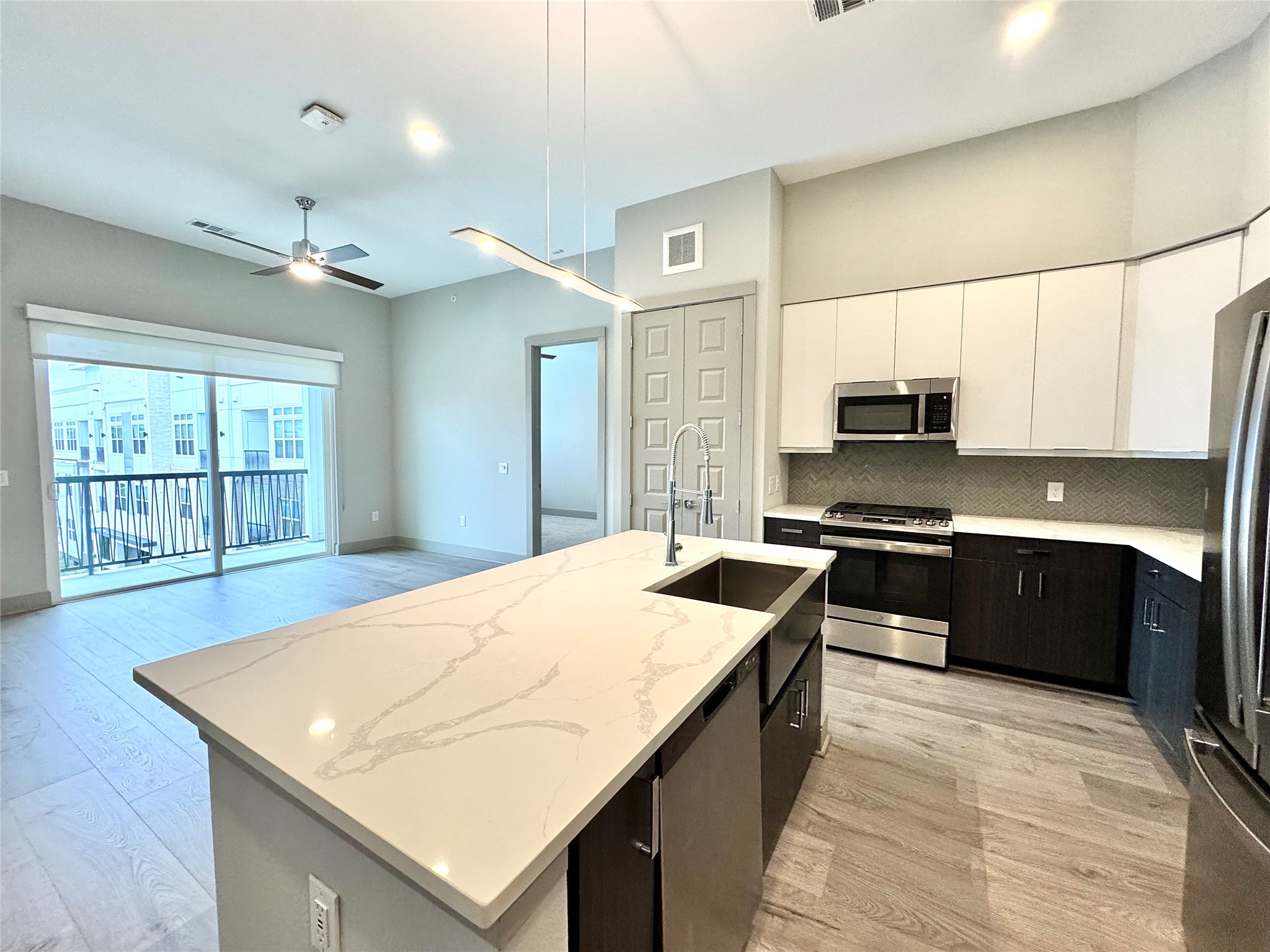 401 West 25th Street, Unit 2125 Houston, TX 77008 - Photo 14 of 33 a kitchen with stainless steel appliances kitchen island a sink dishwasher a stove a microwave oven with white cabinets and wooden floor