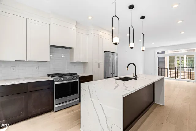 a large kitchen with stainless steel appliances granite countertop a stove a sink a refrigerator and white cabinets with wooden floor